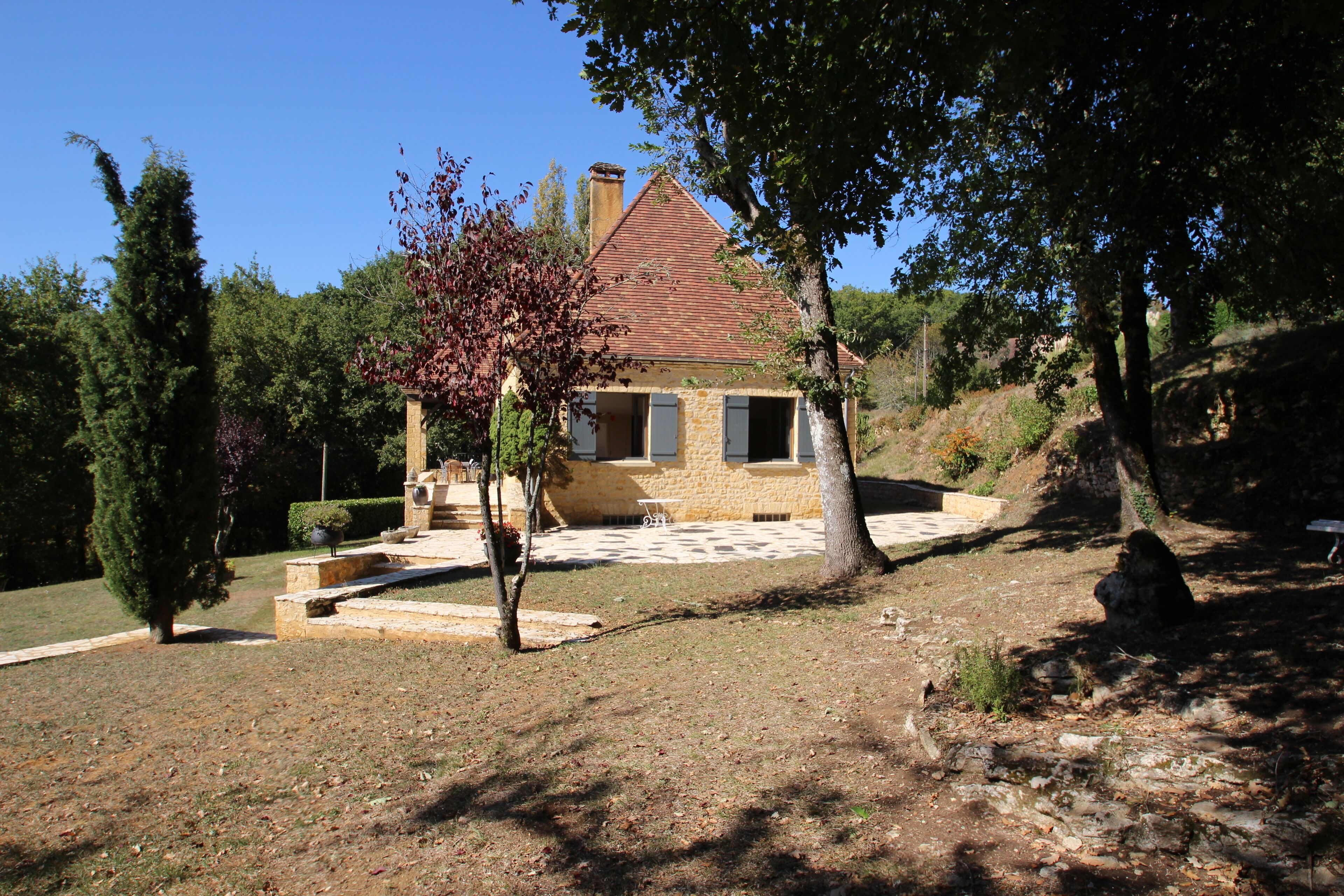 A stone house with a tiled roof, surrounded by trees and a garden.