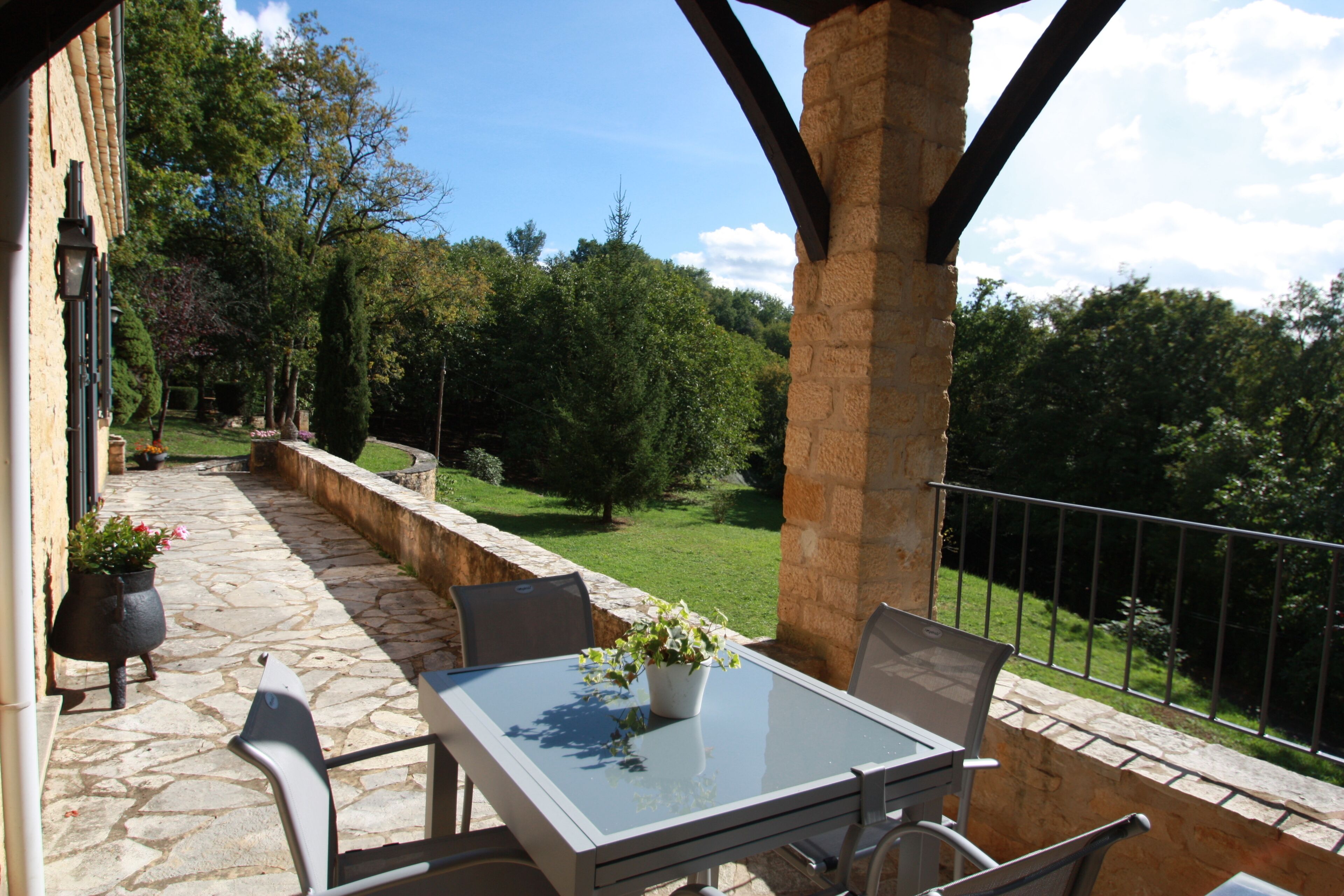 An outdoor patio with a stone floor, a glass table, and chairs. There is a potted plant on the table.