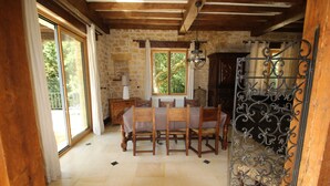 A dining area with a stone wall, wooden ceiling, and a table with chairs. - Charming House in BEYNAC PERIGORD NOIR (Beynac-et-Cazenac)