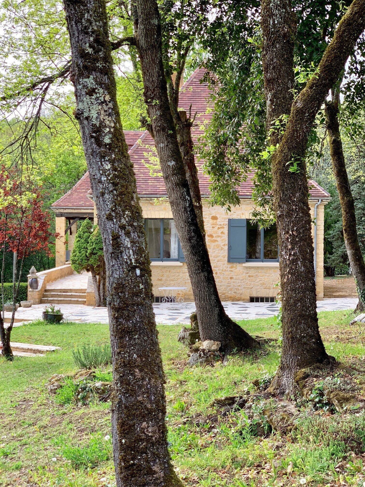 A stone house with a red roof, surrounded by trees and a stone staircase leading to the entrance.
