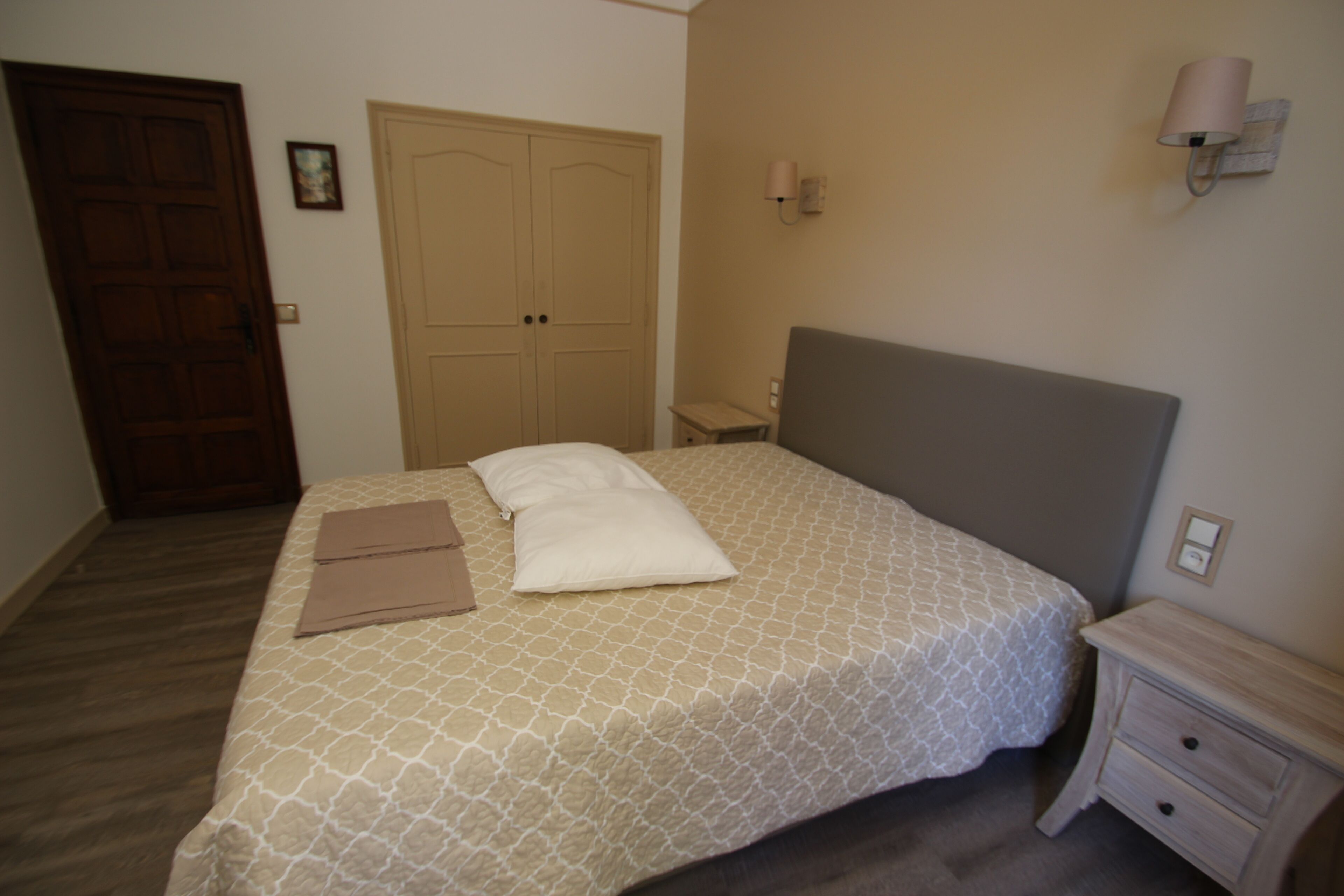 Un dormitorio con cama, mesita de noche, cómoda, puerta y lámpara de pared.