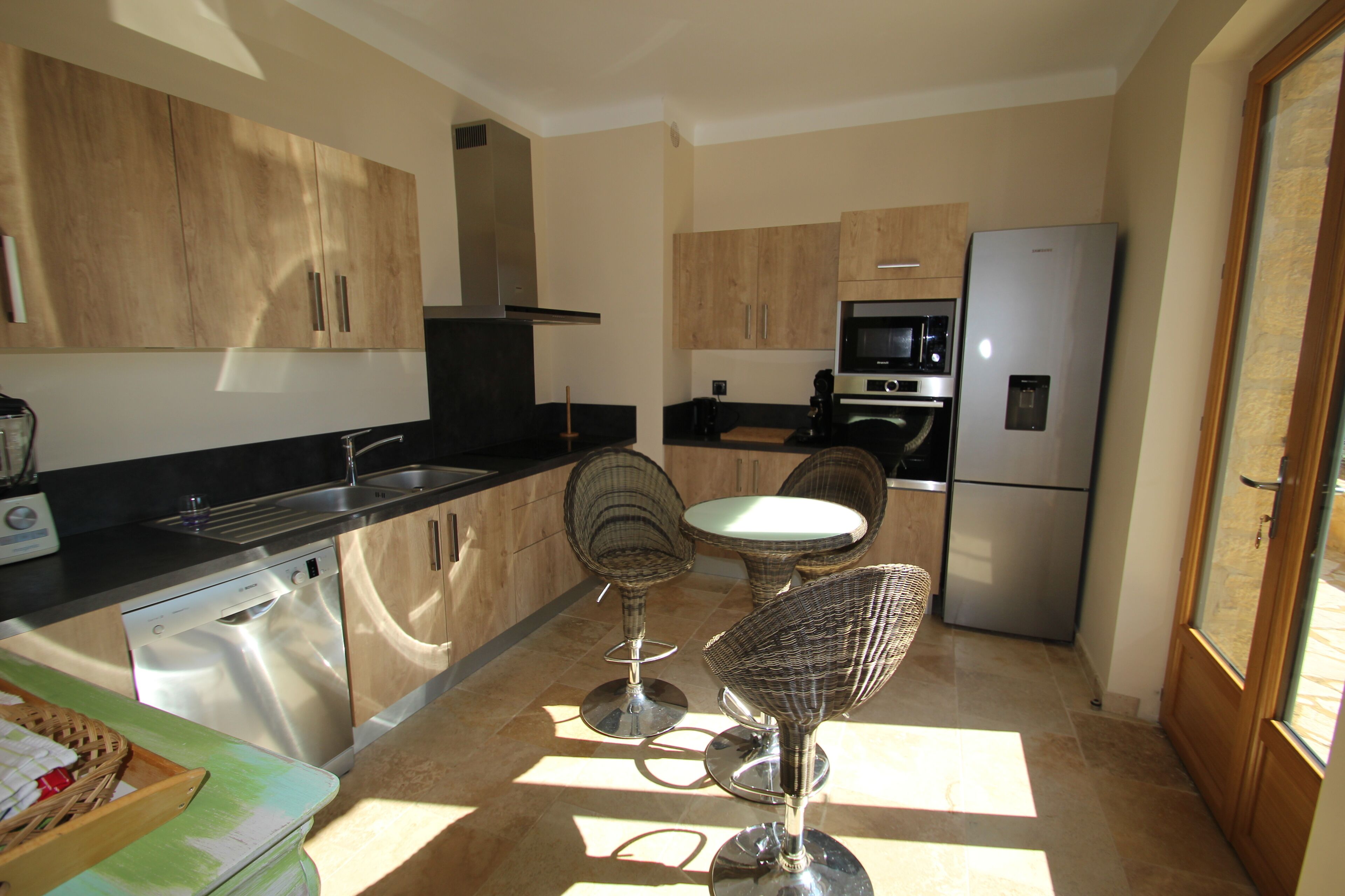 A modern kitchen with stainless steel appliances, wooden cabinets, and two wicker bar stools.