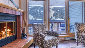 A cozy room with a fireplace, two patterned armchairs, and large windows offering a view of a snowy landscape. - Big 2Br/2 Bath Condo (1443 Sq. Ft.; 2 Living Rooms; Sleeps 10); Walk To Lifts. (Keystone)