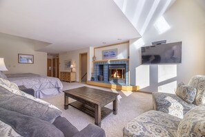 A spacious living room with a fireplace, a television mounted on the wall, and a sofa set.