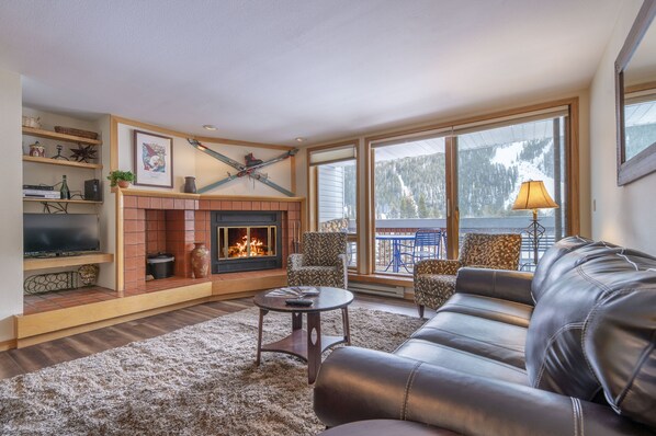 A living room with a fireplace, leather sofa, and a television on a shelf.