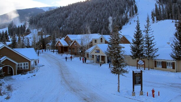 A snow-covered lodge with multiple wooden buildings, a ski slope in the background, and a clear sky. - Big 2Br/2 Bath Condo (1443 Sq. Ft.; 2 Living Rooms; Sleeps 10); Walk To Lifts. (Keystone)