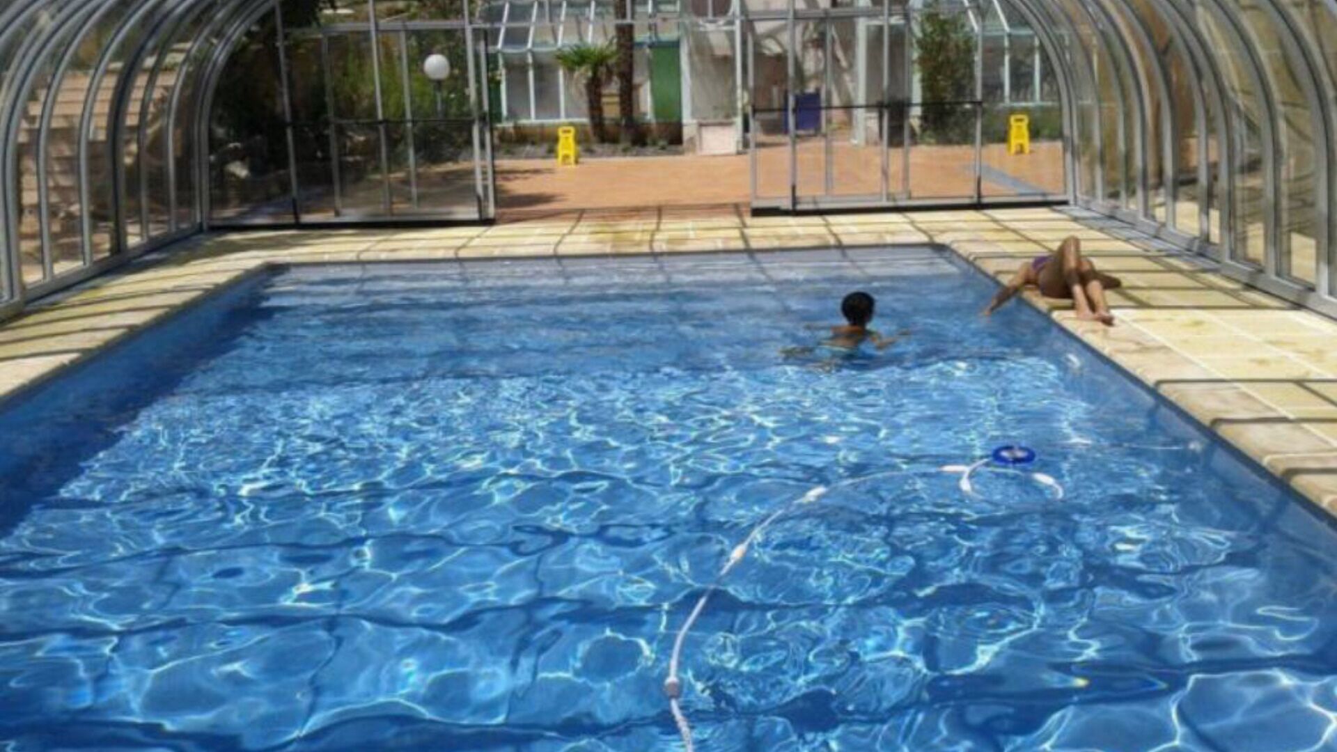 Una piscina con agua azul cristalina, rodeada por una estructura de vidrio.