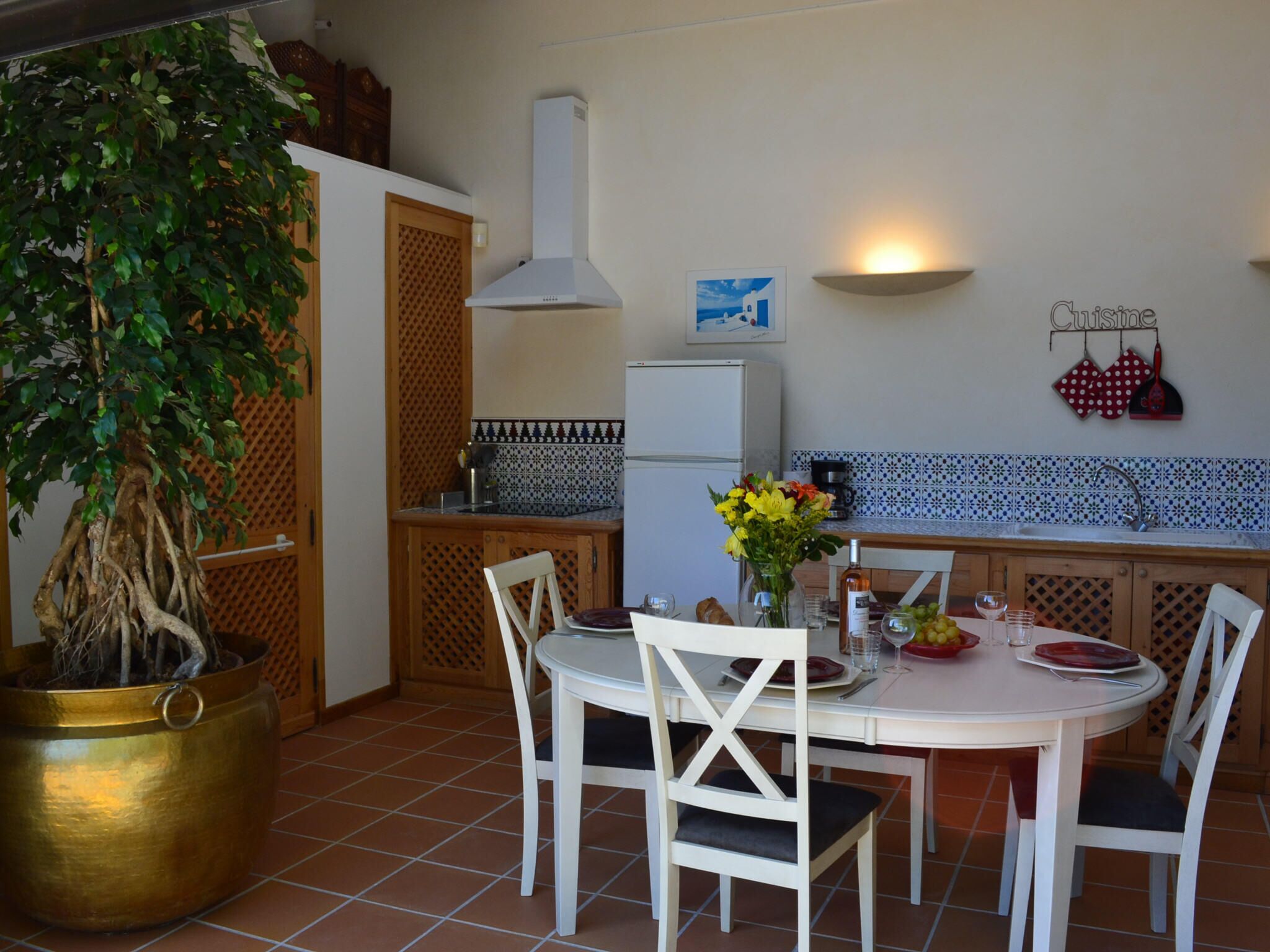 Una cucina con un tavolo da pranzo, sedie, una pianta in vaso e un frigorifero.
