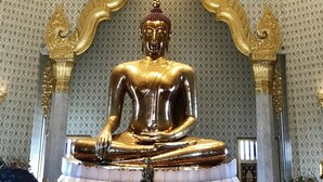 Una gran estatua dorada de Buda en un templo con decoraciones doradas intrincadas y un fondo de pared con diseños.