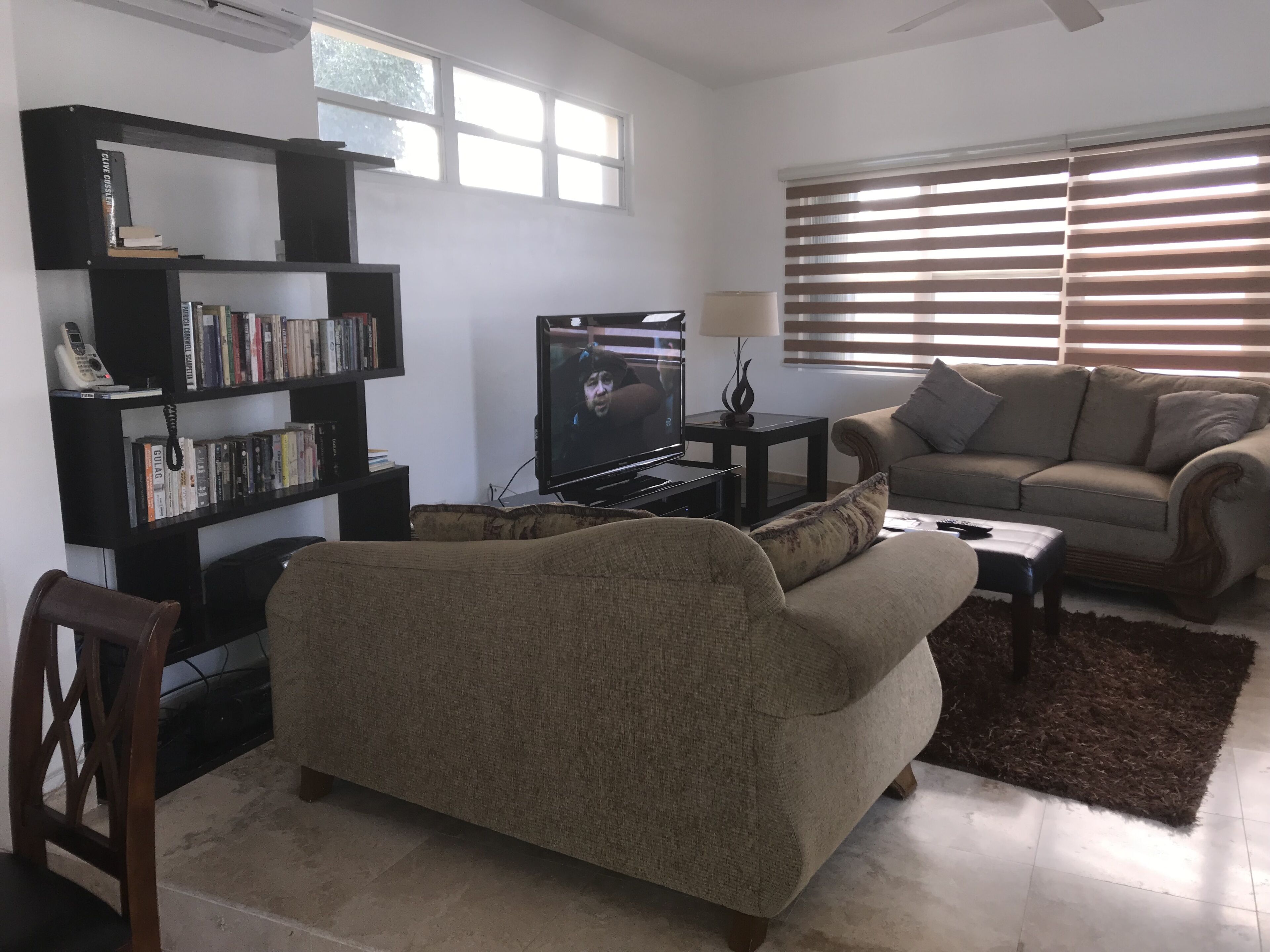 Ein Wohnzimmer mit einer Couch, einem Couchtisch, einem Fernseher, einem Bücherregal und einem Fenster mit Jalousien.
