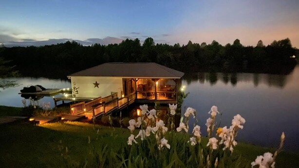 A lakeside lodge with a deck and a star on the roof, surrounded by water and greenery. - Main house & guest cottage on over 400 feet of waterfront on the public side (Mineral)