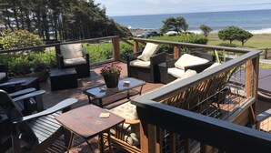 A deck with outdoor furniture, a view of the ocean, and a vehicle parked nearby.