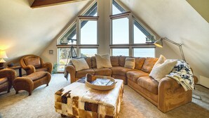 A cozy loft bedroom with a large window, a wooden ceiling beam, a leather sofa, a coffee table, and a lamp.