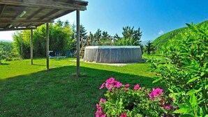 Un espacio al aire libre cubierto con estructura de madera, un área de estar circular y un césped con plantas en flor.