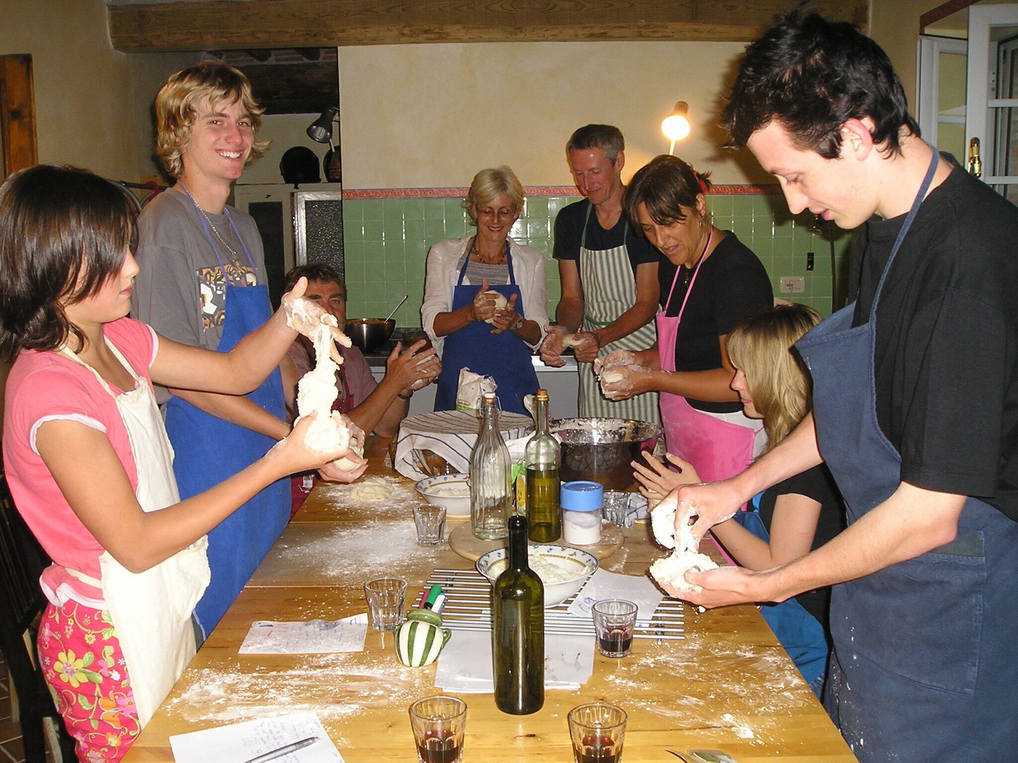 Un grupo de personas participa en una actividad de cocina alrededor de una mesa con harina, una botella y diversos utensilios de cocina.
