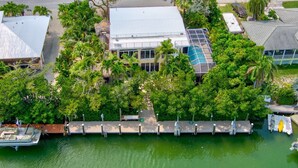 An aerial view of a waterfront property with a dock, a building with a glass facade, and surrounding lush greenery. - Big Kahuna – an expansive and inviting 5-bedroom, 4-bathroom single-family haven that encapsulates the essence of Florida Keys living (Marathon)