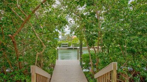 A wooden pathway leading to a dock over water, surrounded by dense foliage. - Big Kahuna – an expansive and inviting 5-bedroom, 4-bathroom single-family haven that encapsulates the essence of Florida Keys living (Marathon)