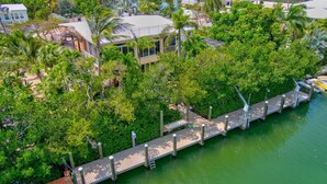 A waterfront property with a wooden dock, lush greenery, and residential buildings. - Big Kahuna – an expansive and inviting 5-bedroom, 4-bathroom single-family haven that encapsulates the essence of Florida Keys living (Marathon)