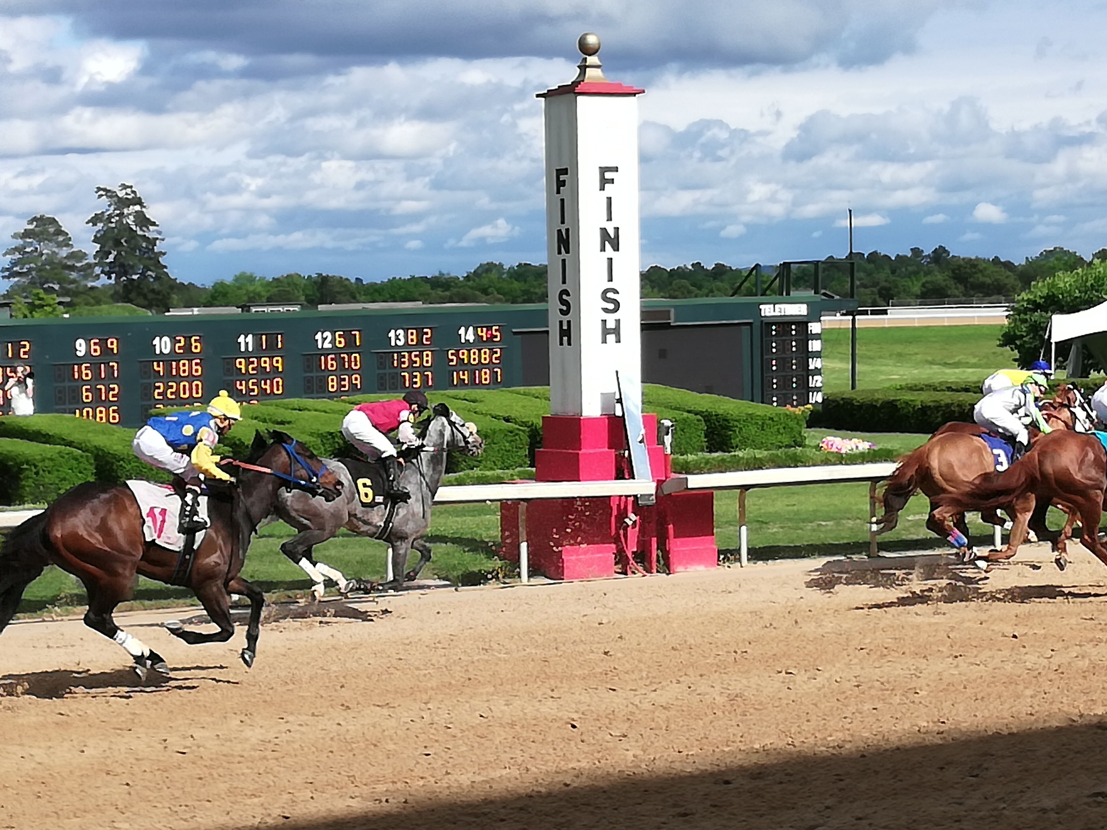 A horse race track with a finish line sign, jockeys on horses, and a digital scoreboard in the background.