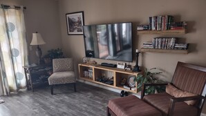 A living room with a TV, bookshelves, a patterned armchair, a wooden coffee table, and a lamp. - CASA LAGO - LAKE FRONT TOWNHOME w/ SPECTACULAR Views w/boat  (Hot Springs)