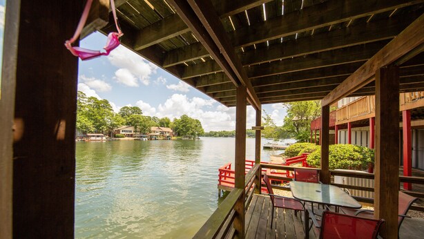 A wooden deck with tables and chairs overlooking a calm river, with buildings in the background. - CASA LAGO - LAKE FRONT TOWNHOME w/ SPECTACULAR Views w/boat  (Hot Springs)