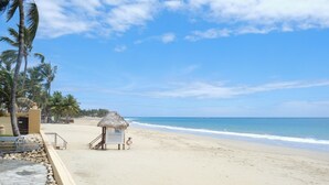 A beach with a thatched-roof hut, palm trees, and a clear sky. - Charming Studio in Ocean Dream (Cabarete)