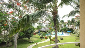 A lush garden with palm trees, a swimming pool, and a thatched-roof structure. - Charming Studio in Ocean Dream (Cabarete)