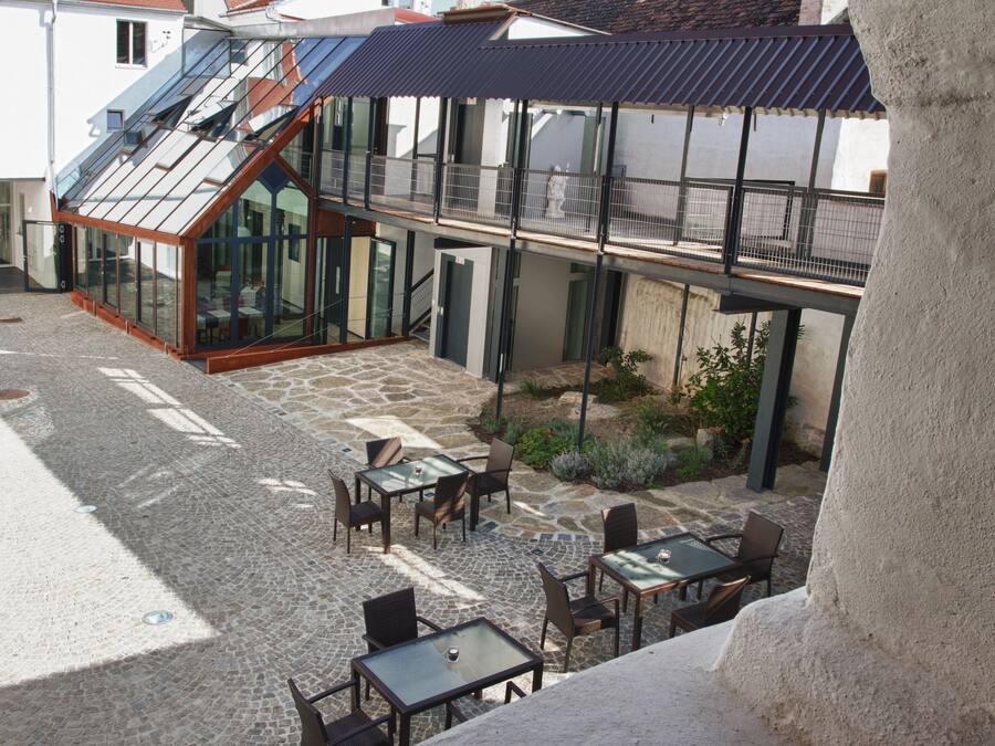 A courtyard with outdoor seating, a glass-enclosed dining area, and a staircase leading to an upper level.