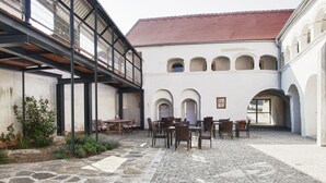 Un patio con suelo de piedra, mobiliario exterior y un edificio con arcos y tejado de tejas rojas.