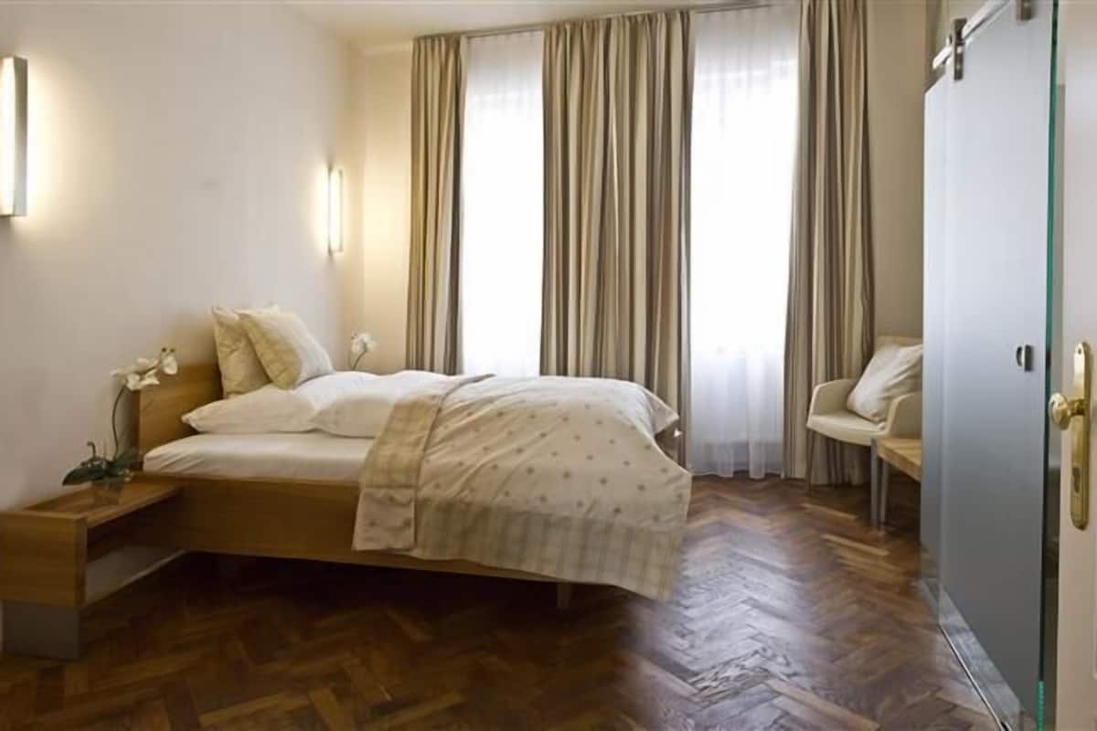 A bedroom with a bed, bedside table, lamp, curtains, and a wardrobe.