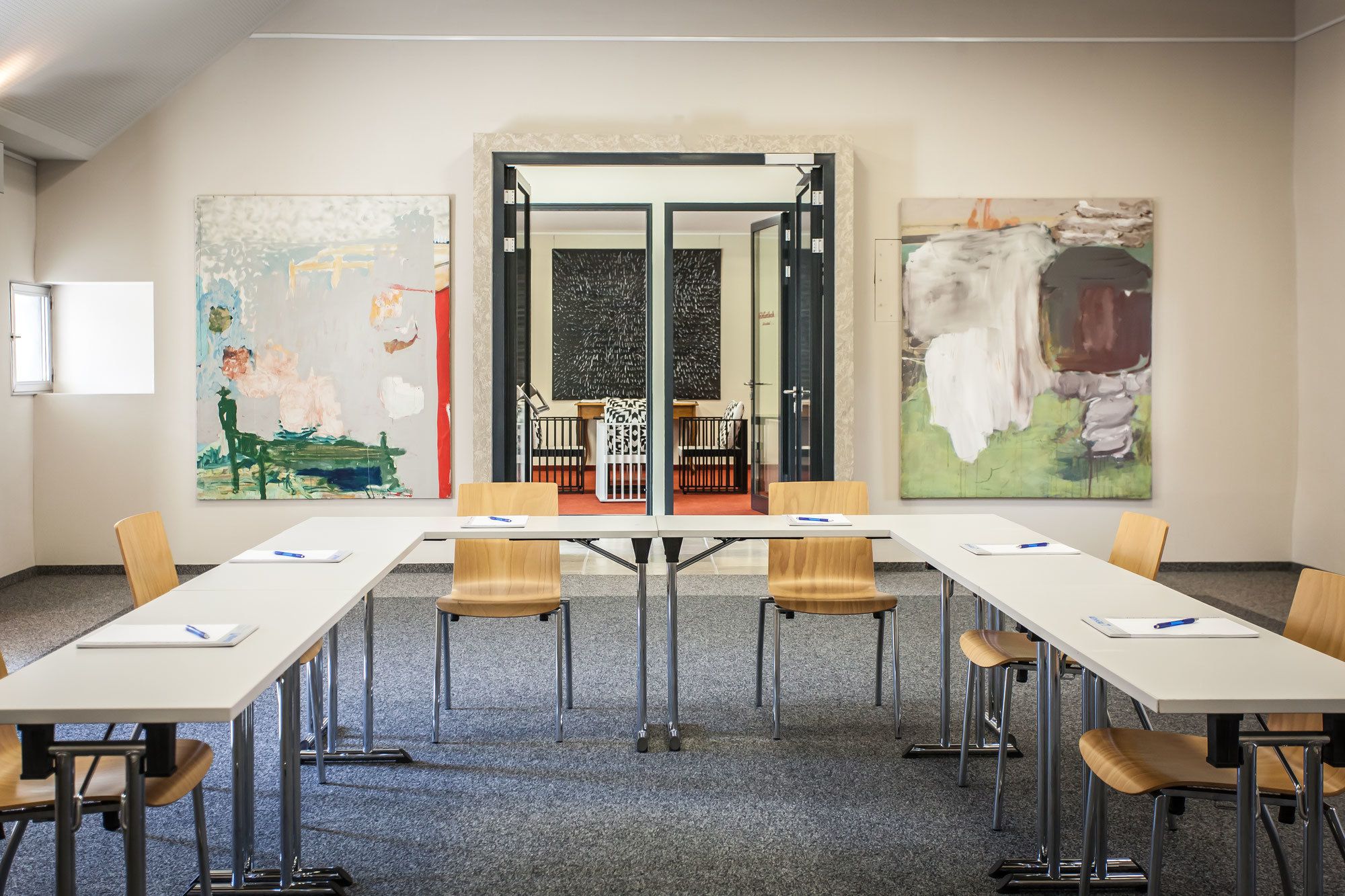 Une salle de conférence avec une longue table, six chaises et des tableaux abstraits accrochés aux murs.
