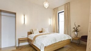 Un dormitorio con cama de madera, mesitas de noche, lámpara de noche, candelabro, ventana con cortinas y un jarrón con flores.