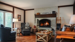 A cozy living room with a fireplace, wooden flooring, and a mix of modern and classic furniture.