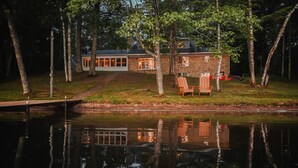 A lakeside cabin with a dock, surrounded by trees, and a pathway leading to the entrance.