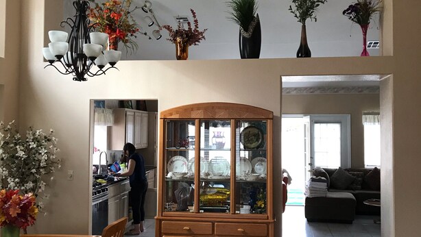 Un amplio salón con una mesa de comedor de madera, sillas, un aparador con puerta de cristal y una cocina al fondo.