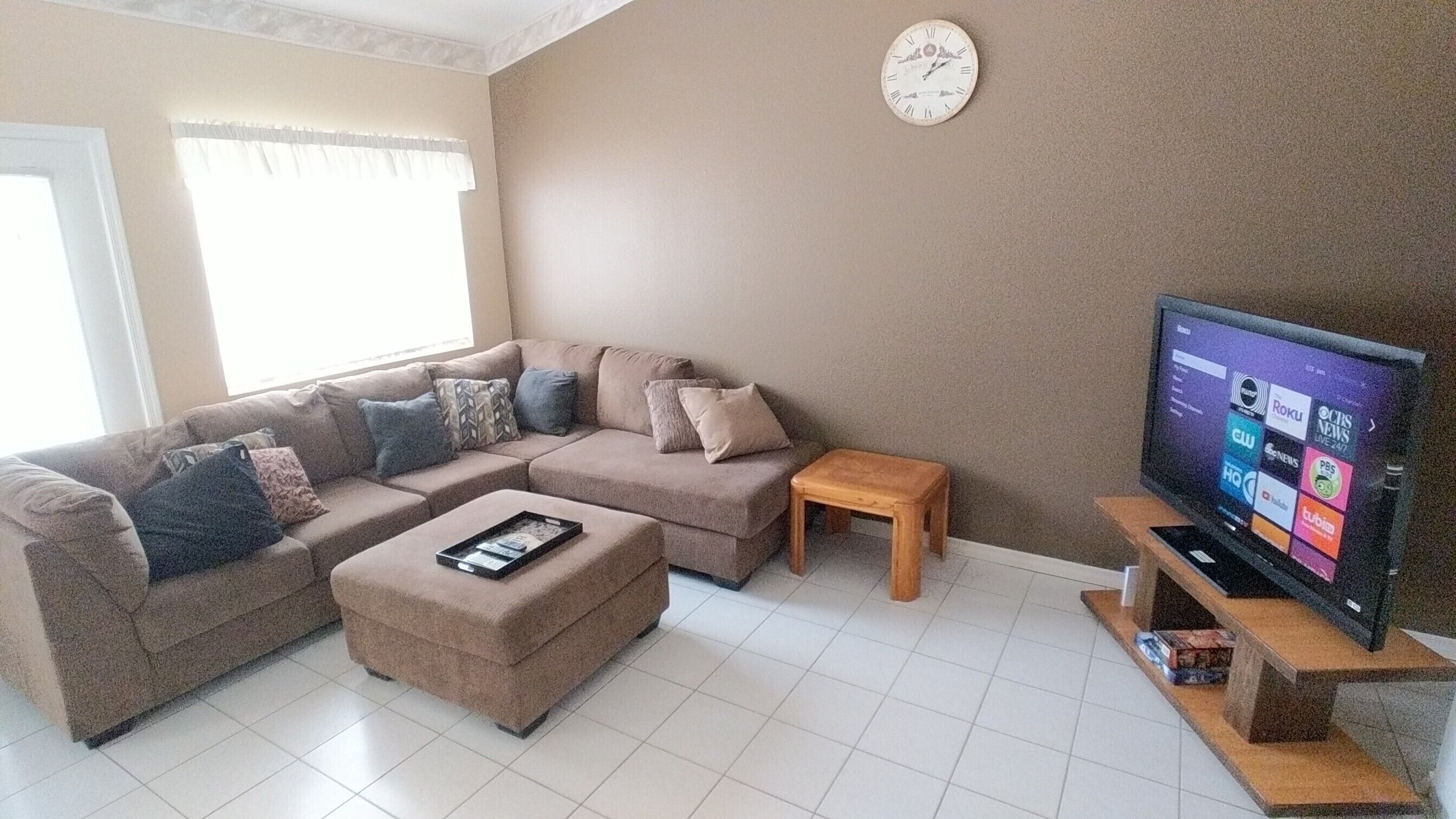 Una sala de estar con un sofá modular, una mesa de centro, un televisor y un reloj en la pared.