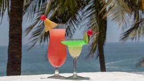 Two cocktails on a table with a beach and palm trees in the background. - Deluxe Beach Front Villa “Tesoro D” (Ixtapa-Zihuatanejo,)