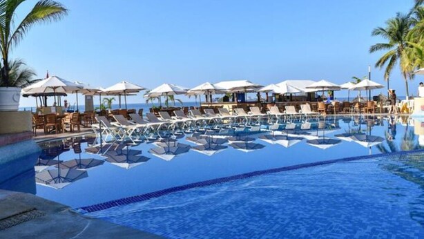 A poolside area with lounge chairs and umbrellas, a clear sky, and a view of the ocean. - Deluxe Beach Front Villa “Tesoro D” (Ixtapa-Zihuatanejo,)