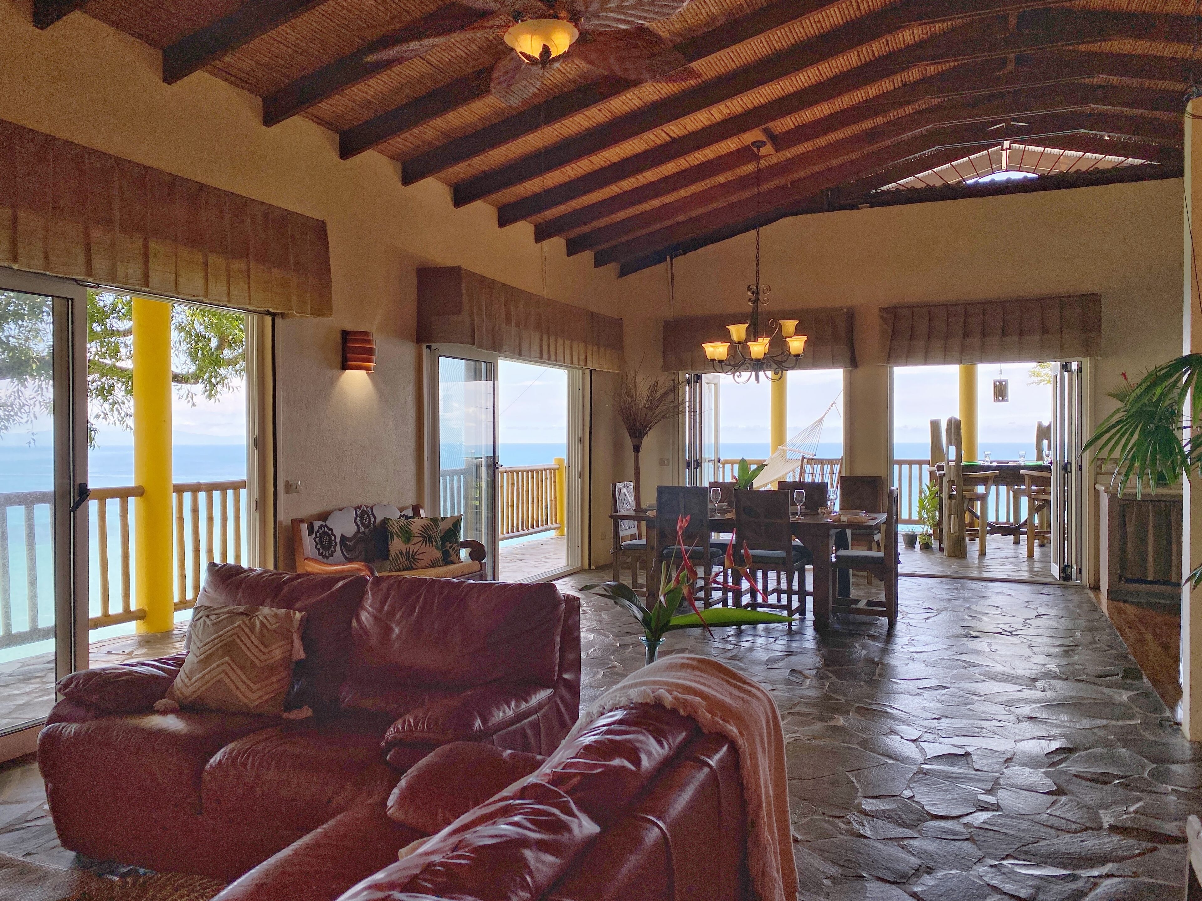 A spacious living area with a stone floor, a red leather sofa, and a dining area with a table and chairs.
