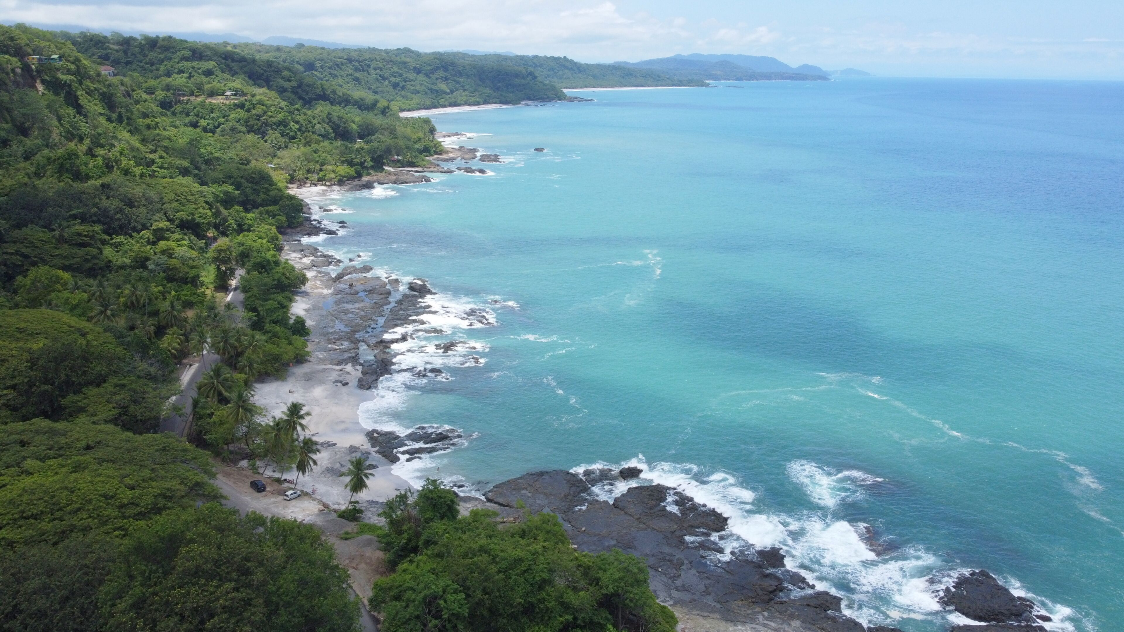 Un paysage côtier comprenant une plage, une côte rocheuse et une végétation luxuriante.