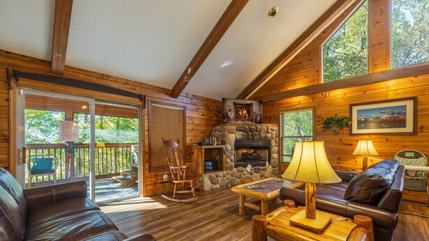 A cozy cabin interior with a stone fireplace, wooden furniture, and a balcony with a view of the forest. - Bluebird Cabin (Hocking Hills area) (Sugar Grove)