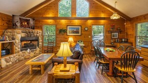 A cozy cabin interior with a stone fireplace, wooden furniture, and large windows. - Bluebird Cabin (Hocking Hills area) (Sugar Grove)