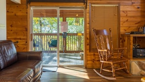 A wooden cabin interior with a sliding glass door leading to a deck, a rocking chair, and a leather couch. - Bluebird Cabin (Hocking Hills area) (Sugar Grove)