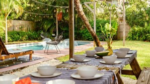 An outdoor dining area with a pool, surrounded by lush greenery and string lights. - Casa del Ojo - 3 King beds - Heated Pool - BBQ - 1 mile to downtown FTL (Fort Lauderdale)