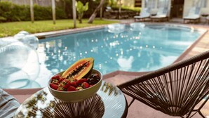 A poolside area with a bowl of fruit, lounge chairs, and string lights. - Casa del Ojo - 3 King beds - Heated Pool - BBQ - 1 mile to downtown FTL (Fort Lauderdale)