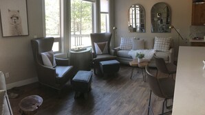 A living room with a dark wood floor, a grey sofa, a grey armchair, a small table, and a mirror on the wall. - Look No Further! Brand New Build in Winter Park/Fraser (Fraser)