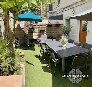 Un patio con tavolo e sedie, circondato da piante in vaso e un recinto in legno.