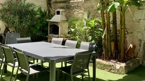 Un patio con una mesa y sillas, rodeado de plantas de banano y un muro de piedra.