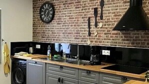 Una cocina con pared de ladrillo, un reloj y una campana extractora negra.
