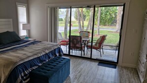 Ein Schlafzimmer mit einem großen Bett, einer Bank, einer Schiebetür zu einer Terrasse mit Stühlen und einem Tisch.